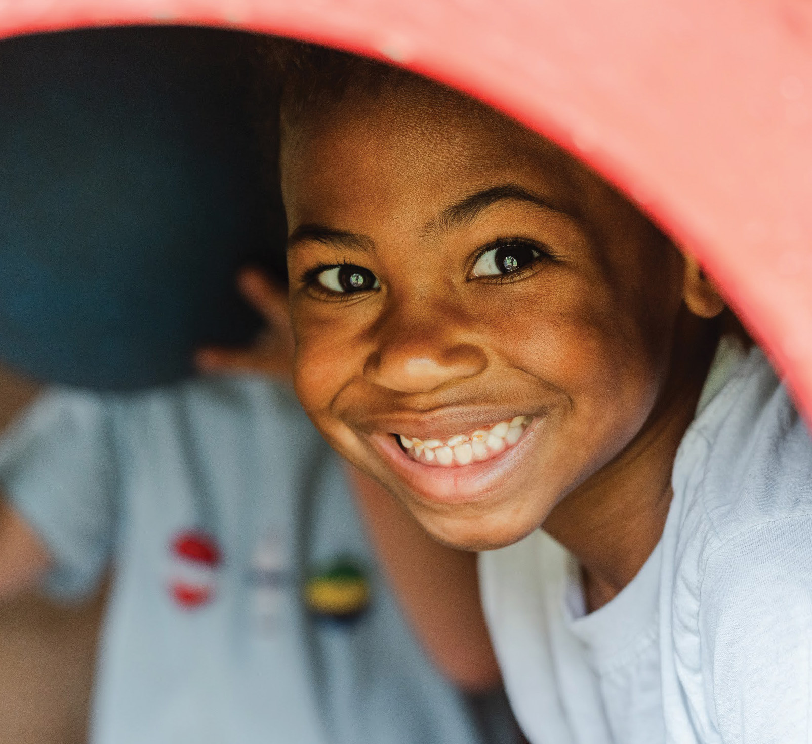 A young child smiles brightly while peering out from under a peach-colored hood.