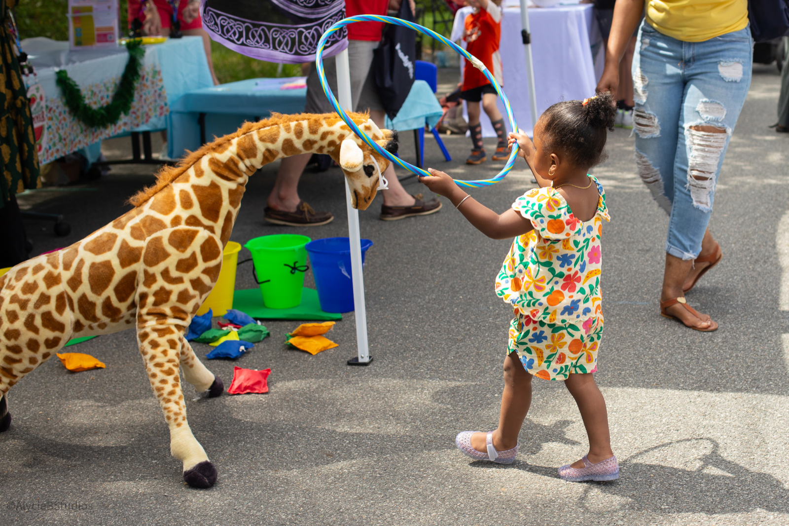 A young child engaged in play with a hula hoop and a giant stuffed giraffe at a ReadyKids community event.