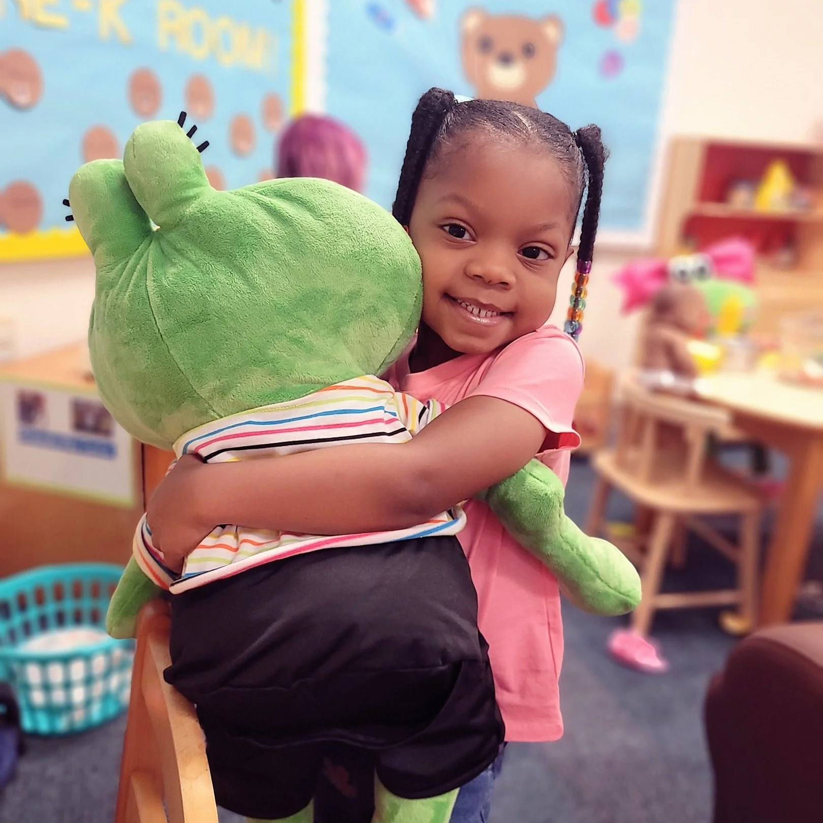 A young child hugs a large stuffed frog at a ReadyKids early childhood program.