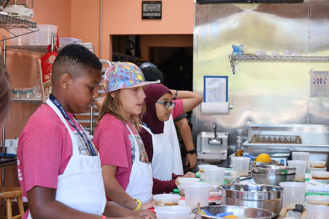Virginia Center for Community Partnerships scholars in aprons prepare food together in a kitchen during a hands-on program session.